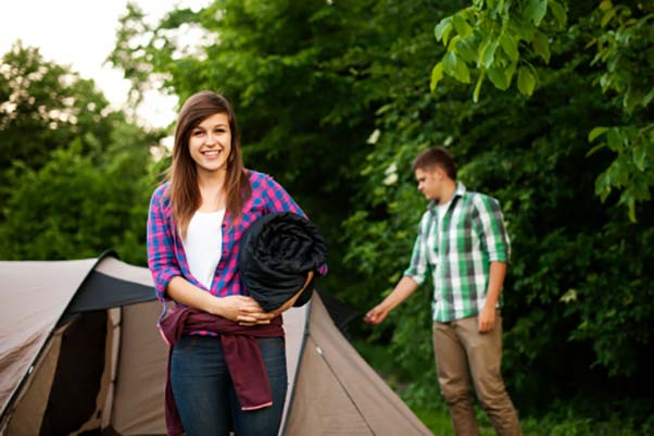 A young woman and man standing next to their tent on a camping trip