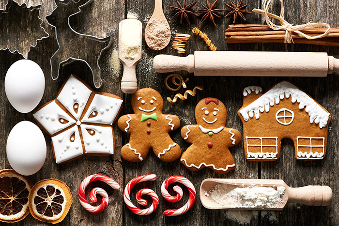 An assortment of Christmas cookies, ingredients, candy canes, eggs, gingerbread men and house, laid out against wooden background