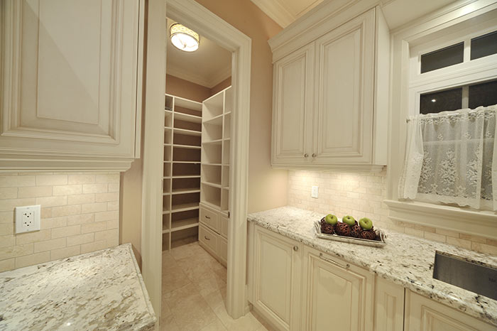 Modern white kitchen with entry to a pantry with multiple shelves for supplies