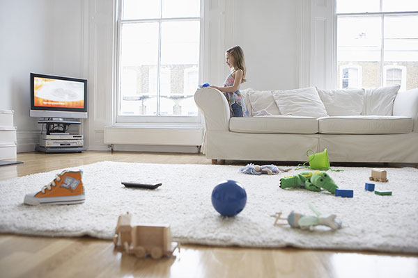 Girl watching the TV while her toys and shoes are scattered all over the floor