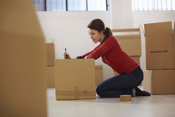 Woman sitting on the floor packing and labeling boxes.