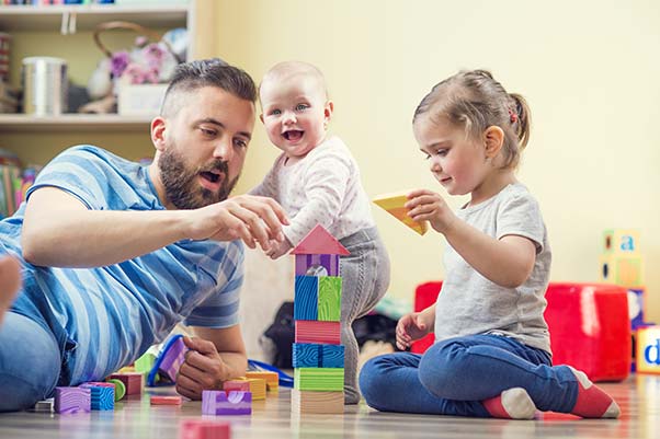 A father and his toddler daughters playing with toys on the floor.