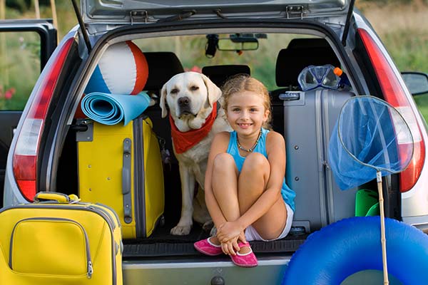 Young girl and her dog sitting in family car packed and ready for vacation.