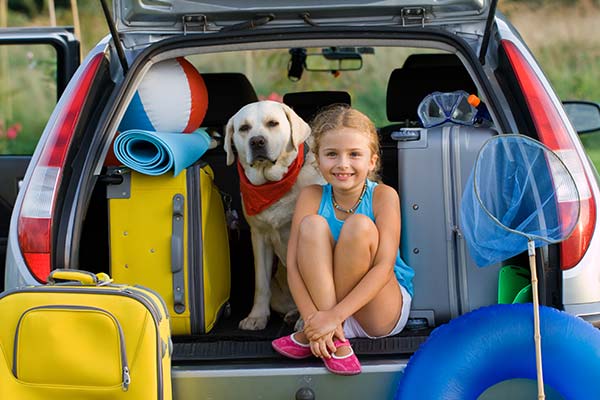 Young girl and her dog sitting in family car packed and ready for vacation.