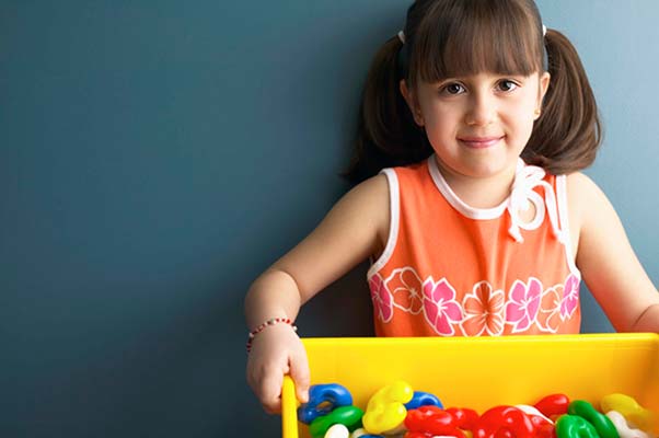 A little girl holds her toys in a bin.