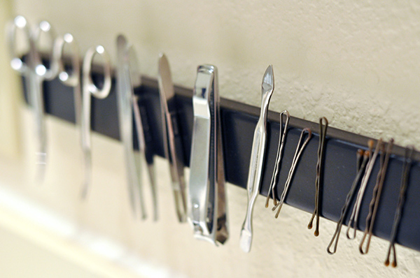 A magnetic strip affixed to the inside of a medicine cabinet door with tweezers, clippers, and other tools neatly stored.