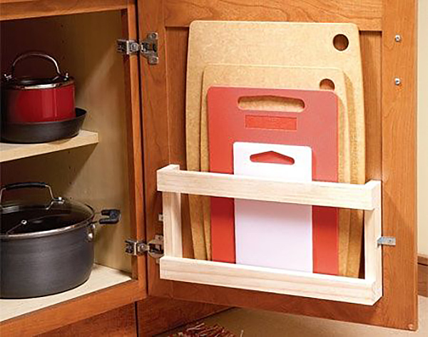 A kitchen cupboard with wooden magazine rack installed to hold cutting boards on the inside of the door.