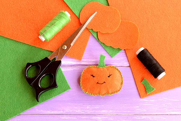 Felt fabric, scissors and thread laid out to make a cutout Halloween pumpkin craft.