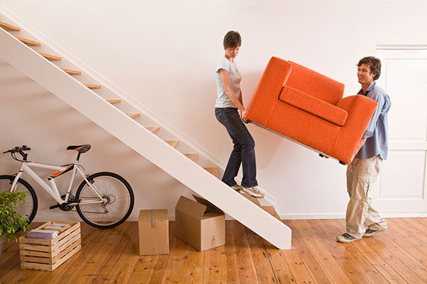 A woman and a man carrying a orange love seat down a flight of stairs while moving out of their home