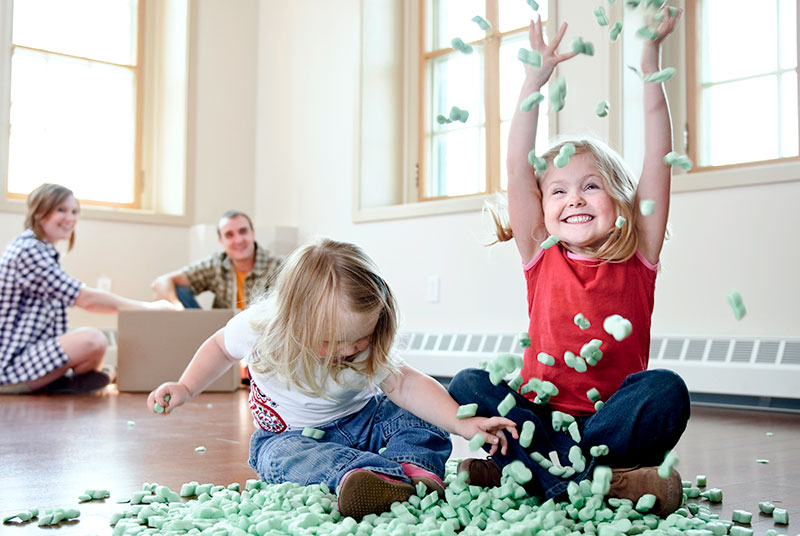 Two toddlers playing with packing peanuts while their parents look on taking a break from packing to move.