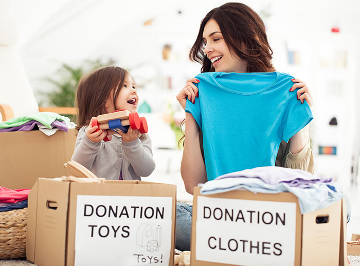 A mom and her young daughter putting toys and clothes into boxes to be donated.