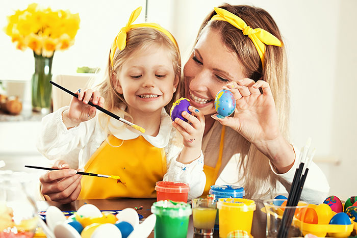 A mom and young daughter decorate Easter eggs with  colorful paint