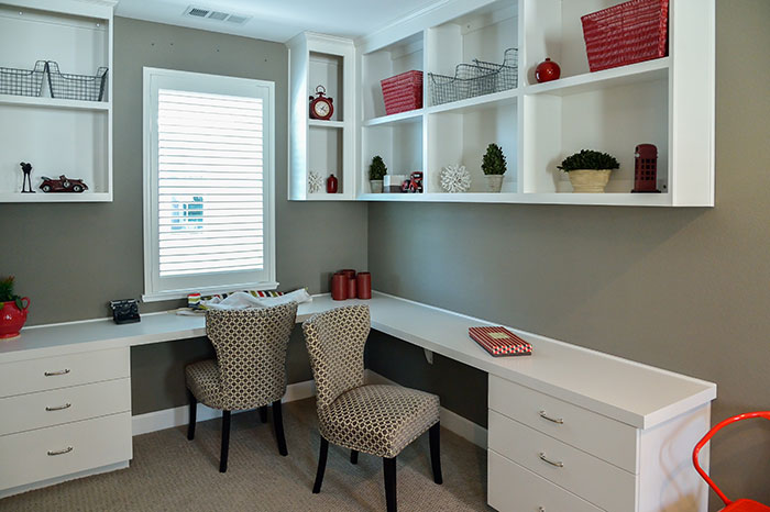 A tidy study with two modern chairs and built-in desk and wall mounted cubbies and shelves with organized items.