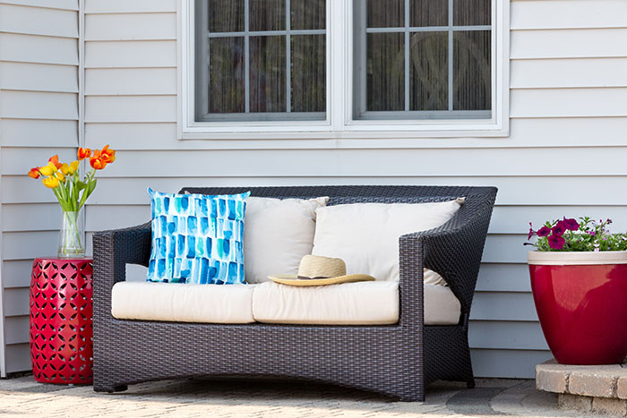 Outdoor garden sofa with colorful throw pillow, flowers in a vase, colorful flowers in pots, arranged on a wooden deck