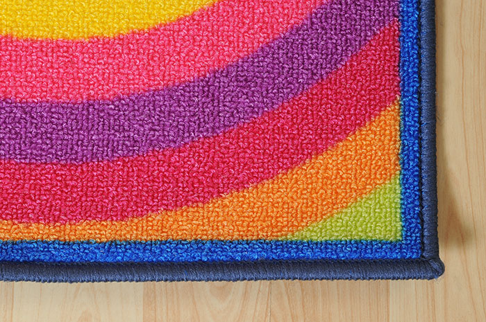 A corner view of a rainbow colored area rug against a wood floor