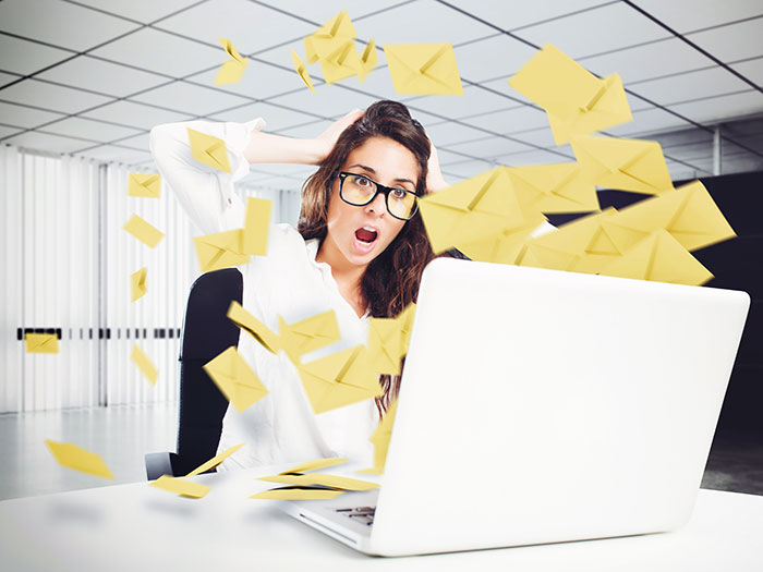 Email clutter concept: a woman sitting in front of her laptop with email envelope icons flying out in disarray, email spam