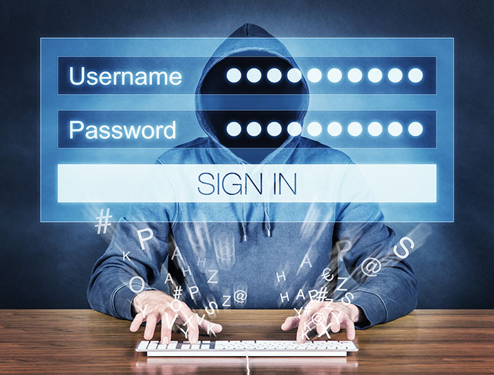 Hacker concept: a man sitting at his computer wearing a hoodie and face concealed, typing a on a keyboard with password related icons flying around