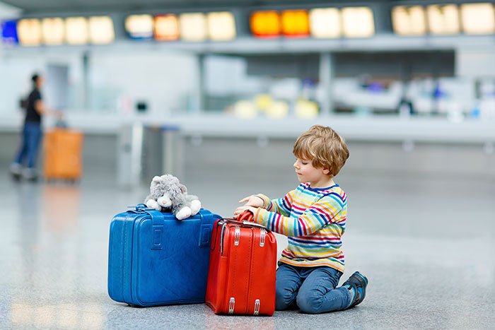 Young boy sitting in the airport with his own luggage and stuffed animal waiting for a flight with his family