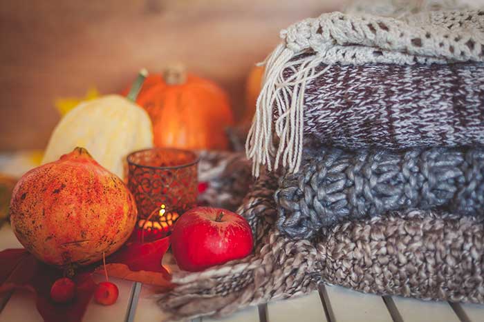 Fall home decor: knitted throw blankets, gourds, pumpkins and spice candle in autumn gold, red, orange hues