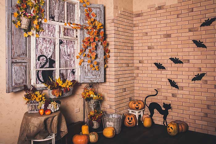 Brick house with Halloween decorations: old shutters, carved pumpkins, black cat silhouette, black bats and harvest baskets and decor