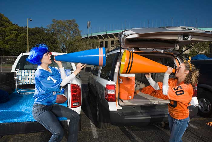 Two cars parked in a stadium lot, two women tailgaters with megaphones - rival tailgaters