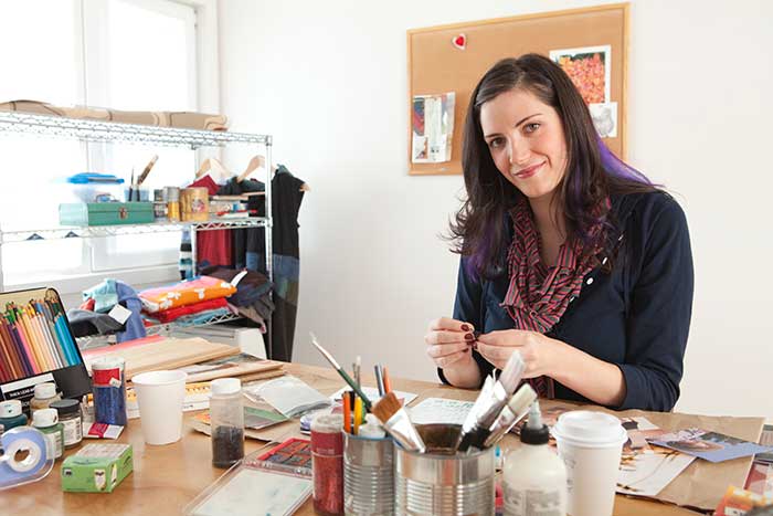 Young woman sitting at a desk doing crafts in her craft room