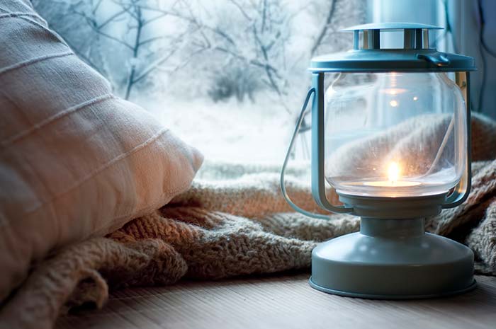 Cozy throw blanket and pillow with a warm lantern  on a wintery windowsill