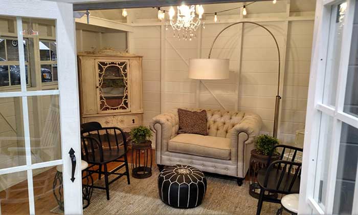 A she shed decorated with cozy sofa, chairs, lighting and footstool