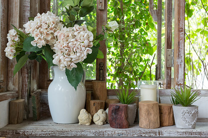 Rustic window with white vase of hydrangea, wood pieces and spring chick figurines, green plants and candles