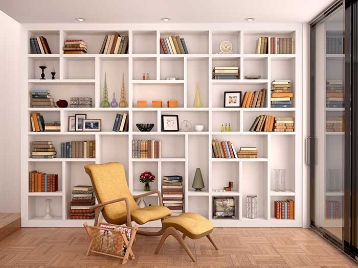 Floor to ceiling white built-in bookshelf filled with books and knick knacks behind a reading chair with footstool 