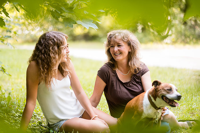 Teenage girl and her dog with her mom sitting in a grassy park meadow