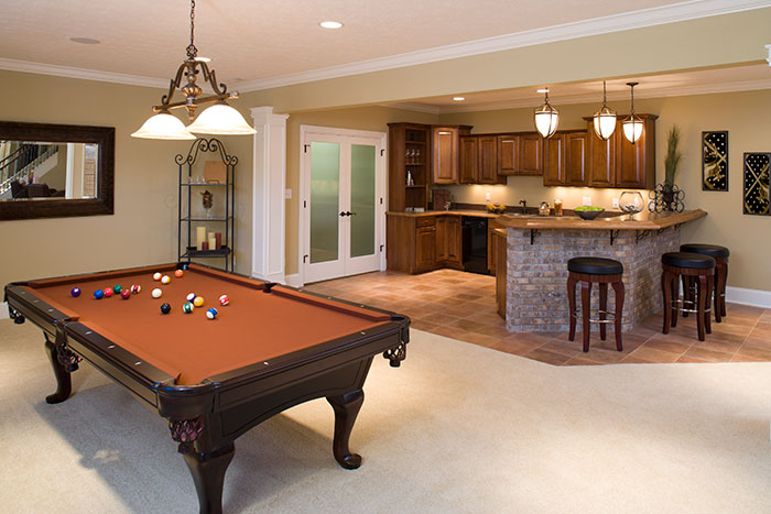 A beautiful man cave with modern lighting, pool table, and a full bar with seating.