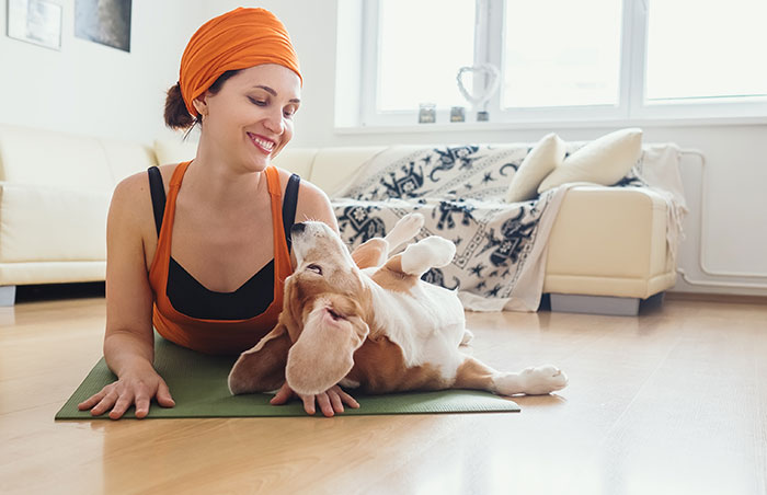 A woman practicing yoga in baby cobra pose with her beagle dog nearby