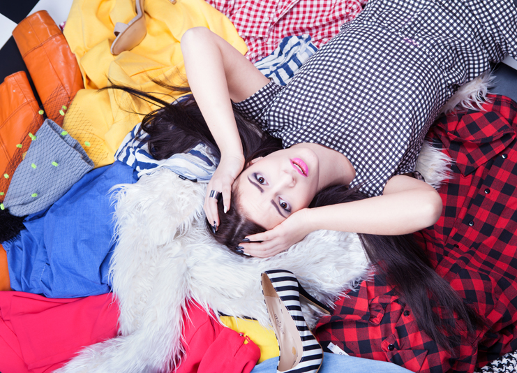 Nothing to wear concept, young attractive stressed woman lying down on a pile of clothes