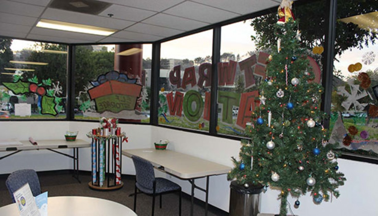 Rolls of gift wrap, Christmas tree, and other holiday decor for the seasonal gift wrapping station in the office