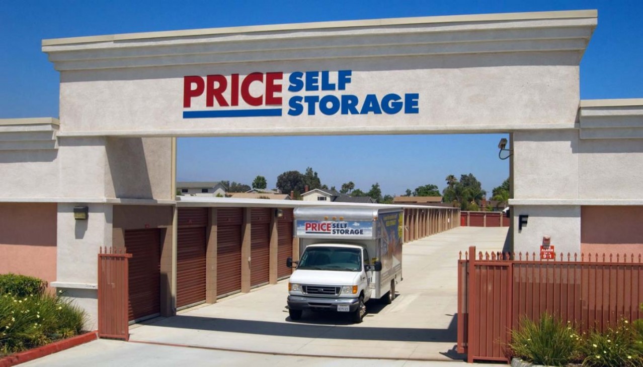 Moving truck driving through the exit gate beneath the Price Self Storage monument sign