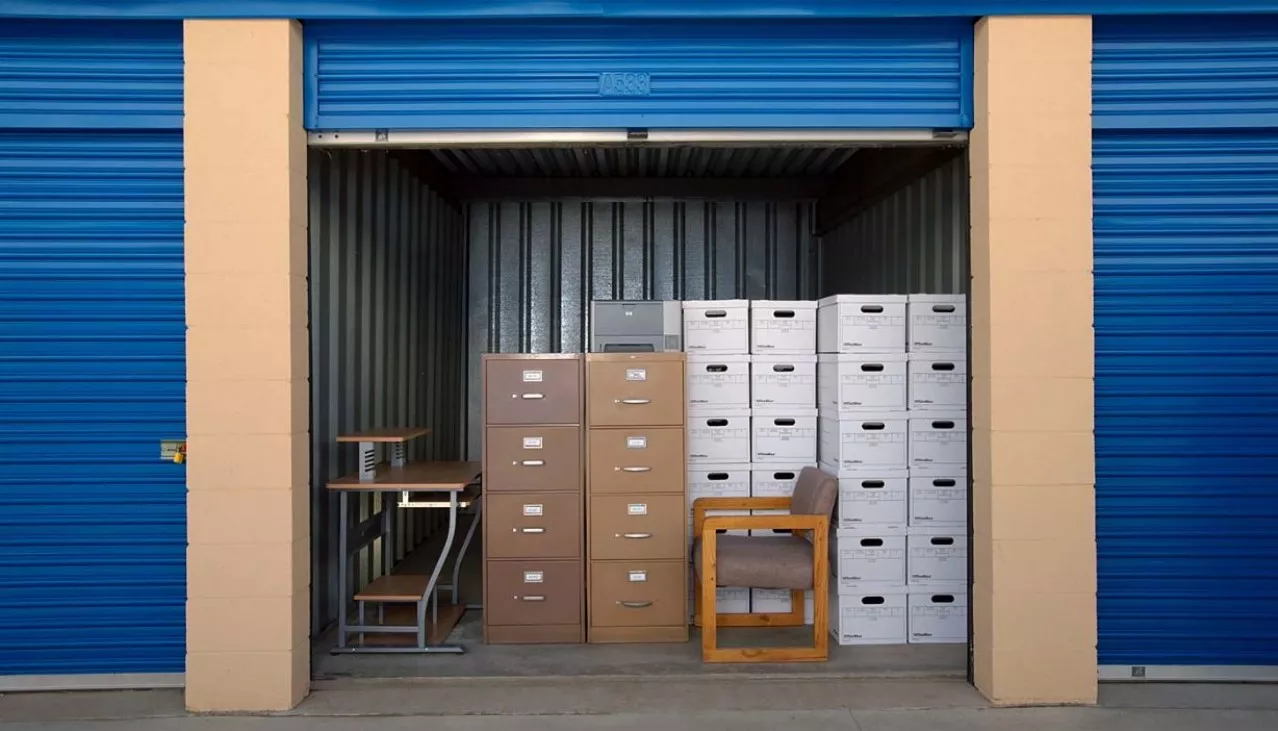 Drive up storage unit with office chairs and boxes stacked inside with door rolled up